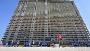 A high-rise building with multiple balconies and a beach area with sun loungers and umbrellas.
