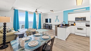 A modern living room with a dining area, kitchen, and balcony with blue curtains.