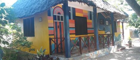 Uma casa colorida com telhado de palha, um pequeno alpendre e uma porta com design colorido.