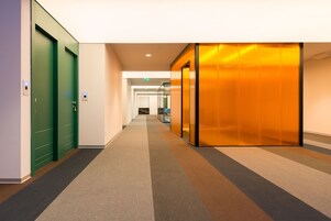 Een moderne hal met groene deuren, een kamerbreed tapijt met patroon en een glazen lift.