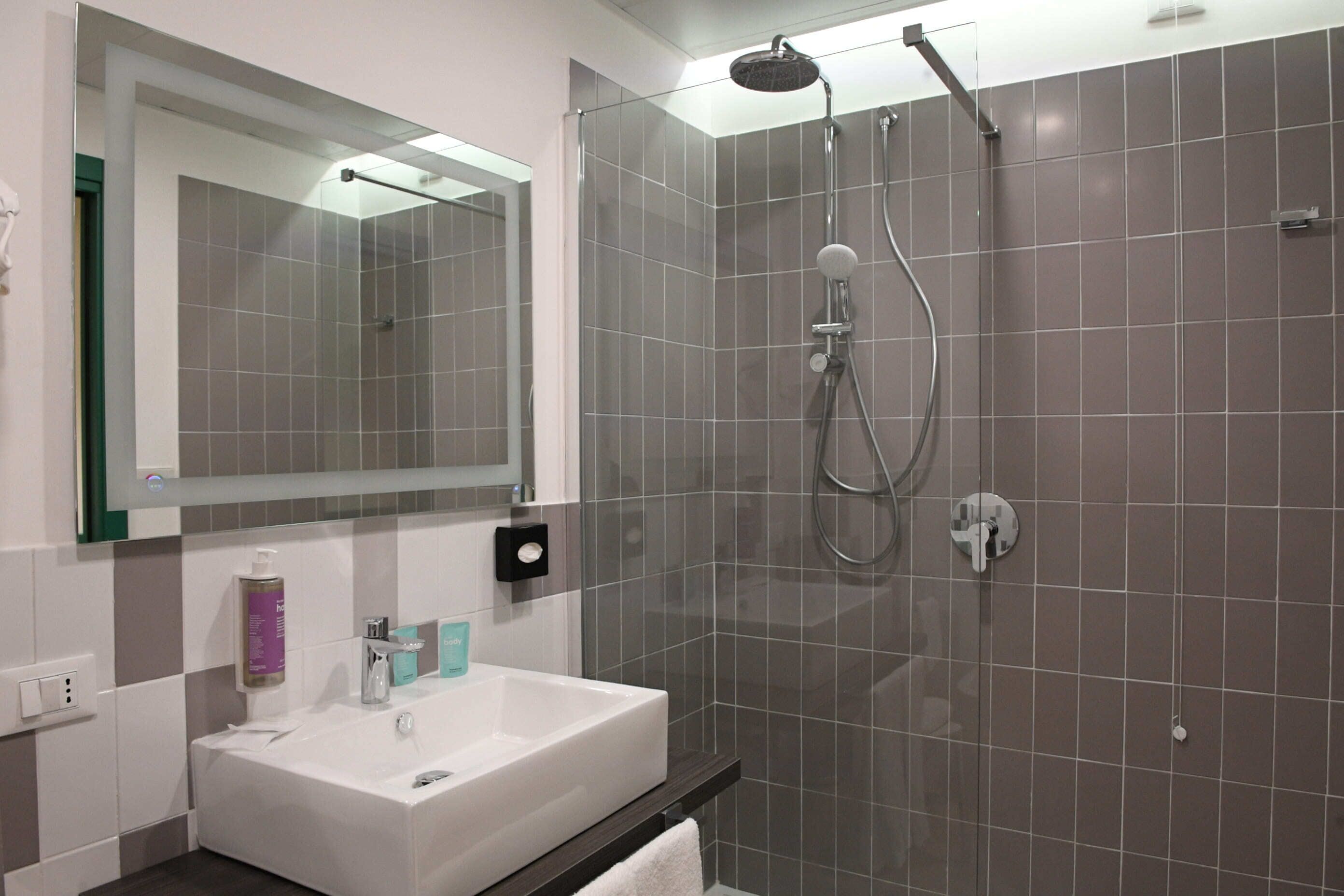 A modern bathroom with a white sink, a large mirror, and a glass-enclosed shower area.