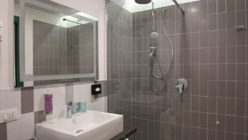 A modern bathroom with a white sink, a large mirror, and a glass-enclosed shower area.