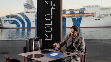 Un uomo seduto a un tavolo con un laptop e un bicchiere d'acqua, con una grande nave sullo sfondo.