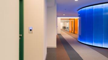 A modern hallway with a green door, a digital display showing the number 207, and a curved blue wall.