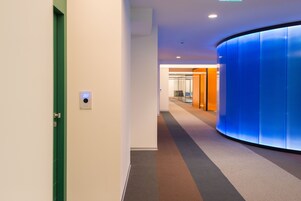 A modern hallway with a green door, a digital display showing the number 207, and a curved blue wall.
