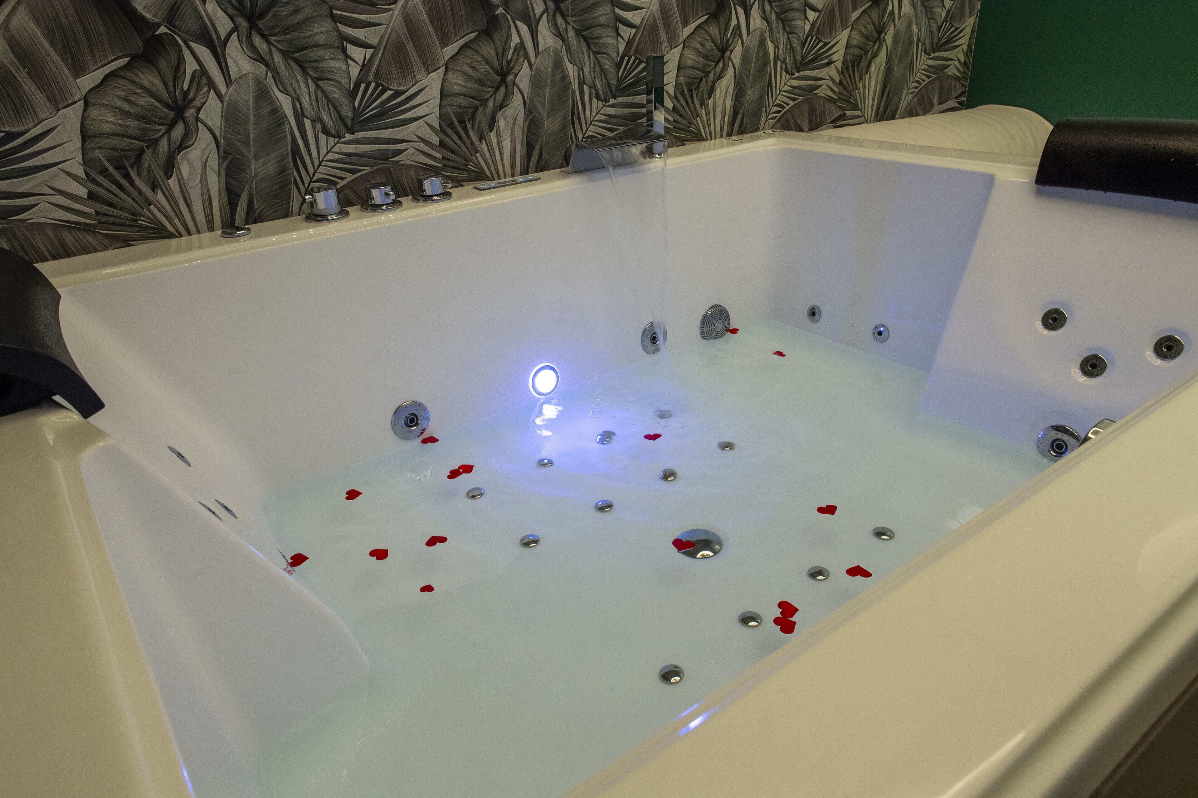 Una bañera con jets de hidromasaje, pétalos de rosa y un grifo moderno.