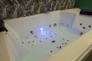 Una vasca da bagno con idromassaggio, petali di rosa e un rubinetto moderno.