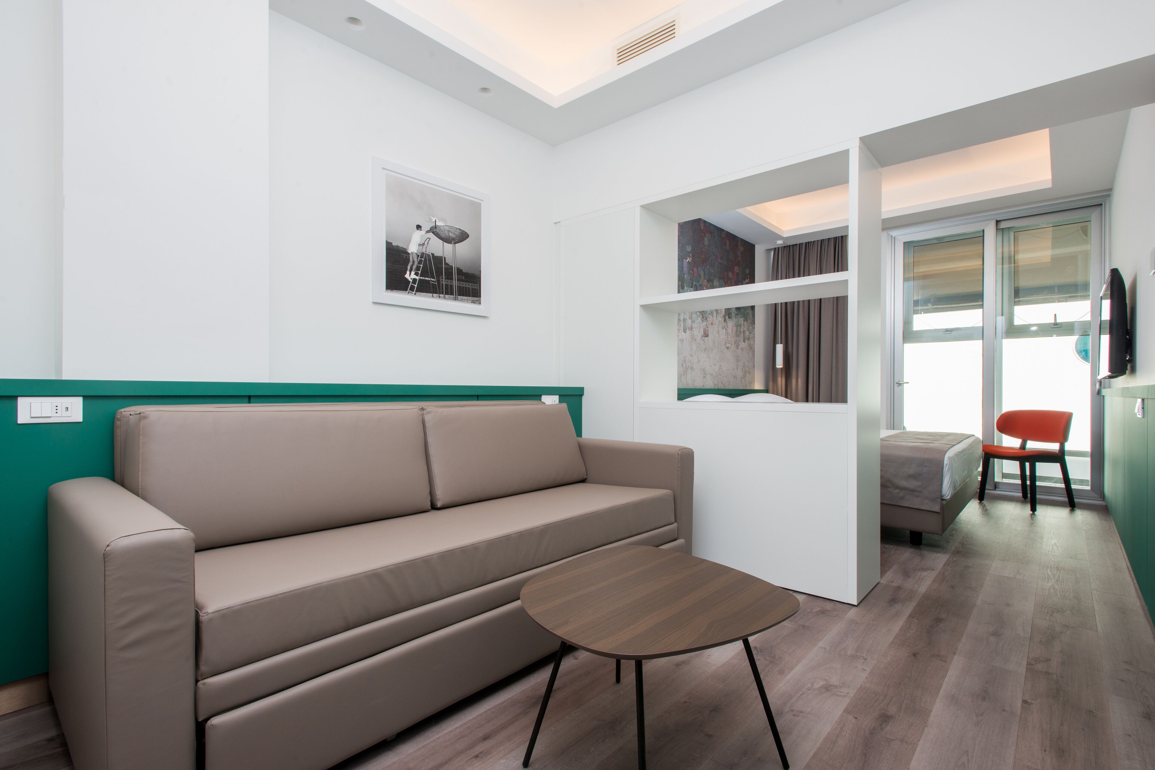 A modern room with a beige sofa, a small wooden table, and a view of the outside through a glass door.