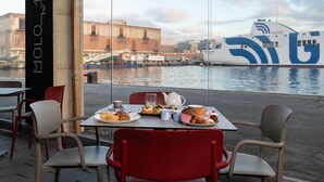 Una mesa con desayunos, sillas rojas y vista a un barco grande con colores azul y blanco.