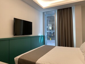 Een hotelkamer met een bed, een wandtelevisie en uitzicht op de straat door een glazen deur.