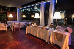 Zona pranzo con un tavolo lungo apparecchiato per un pasto, circondato da sedie e ampie finestre con tende.