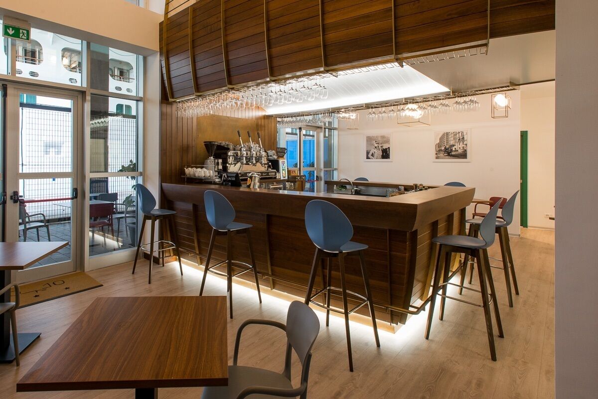 Zona de bar moderna con mostrador de madera, taburetes y una máquina de café.