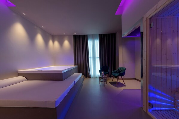 A modern bedroom with a large bed, a small seating area, and a wooden panel wall.