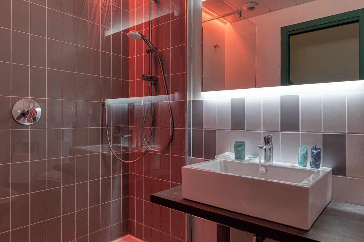 Un baño moderno con ducha envuelta en vidrio, un lavabo blanco con dos grifos y un espejo sobre el lavabo.