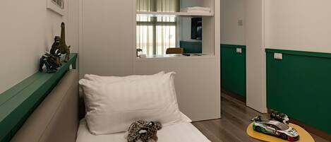 A small, compact room with a bed, a green bench, a small table with toys, and a mirror.
