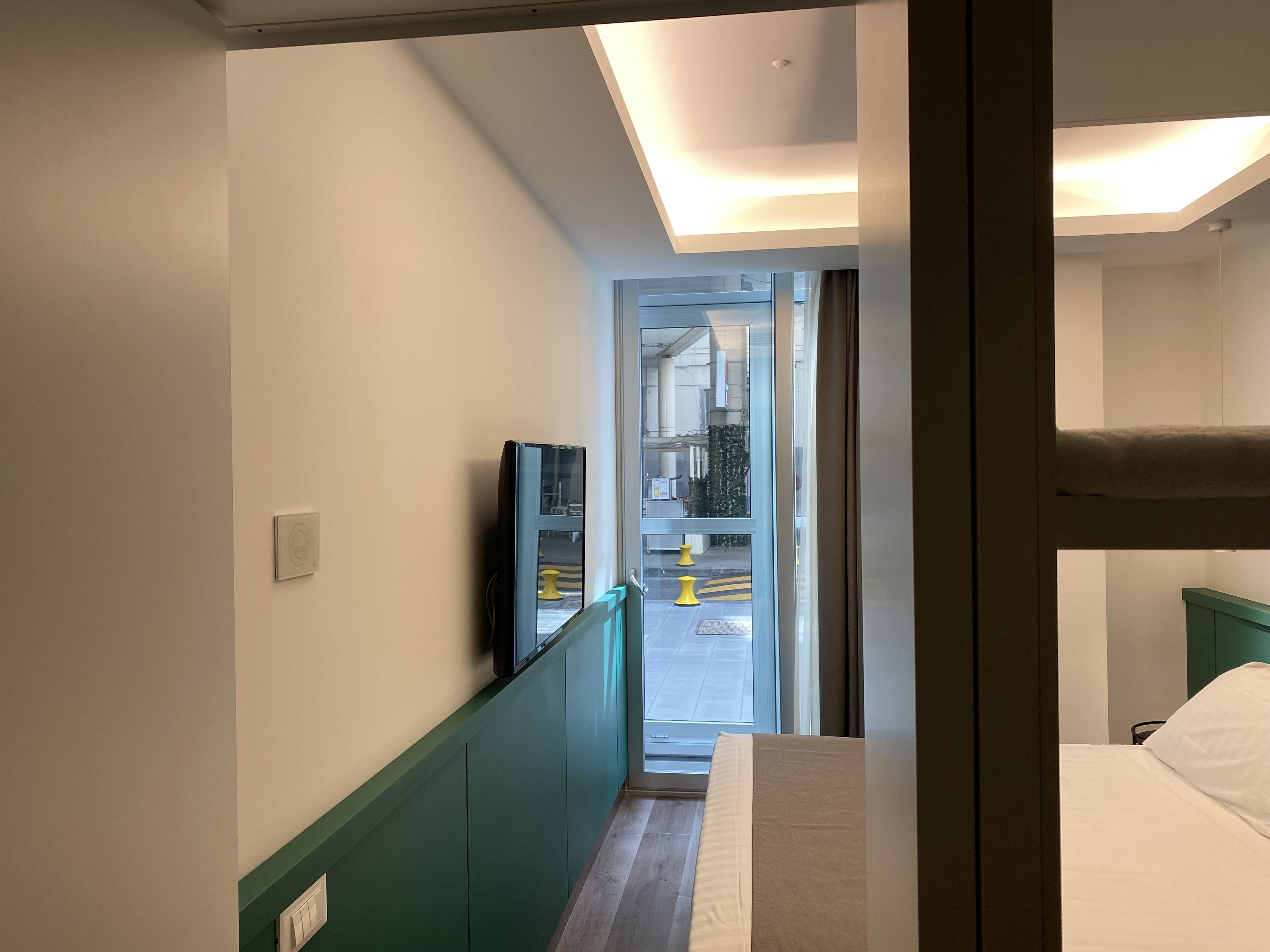 A hotel room with a bed, a TV, and a view of the outside through a glass door.