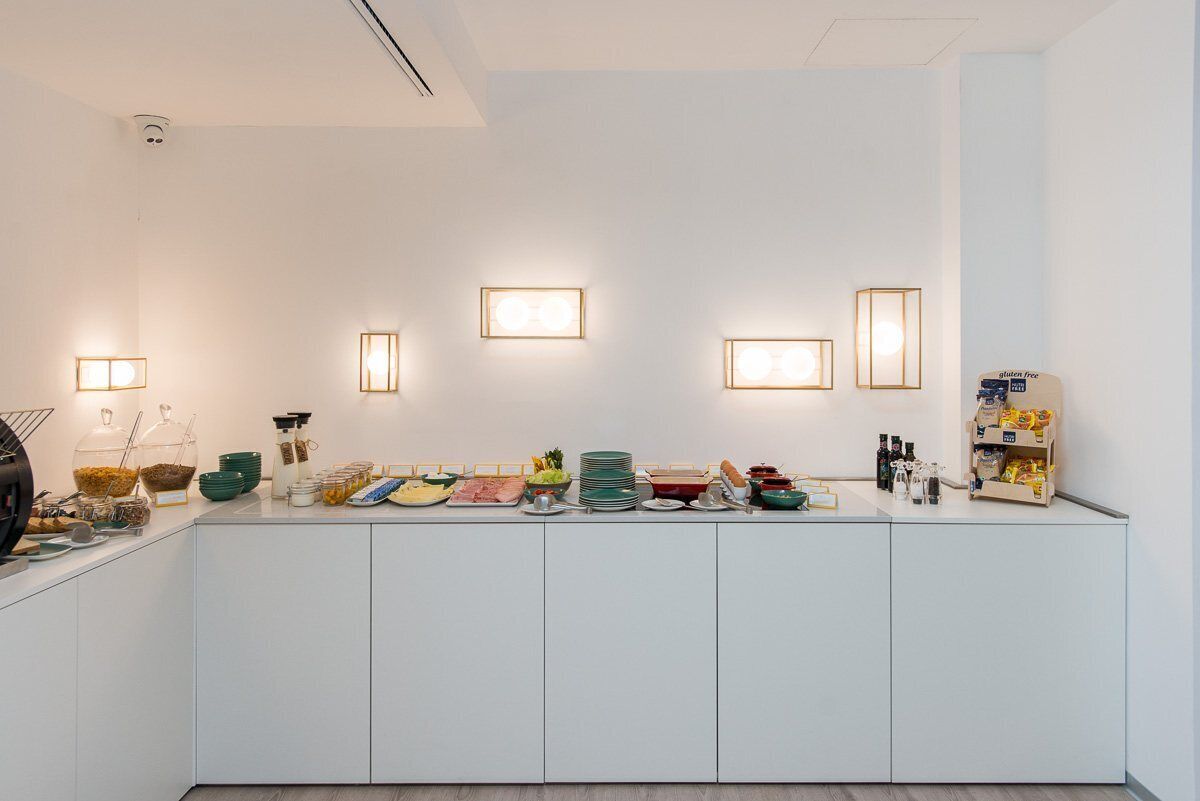 A modern kitchen with white cabinets, a countertop with various food items and utensils, and wall-mounted light fixtures.
