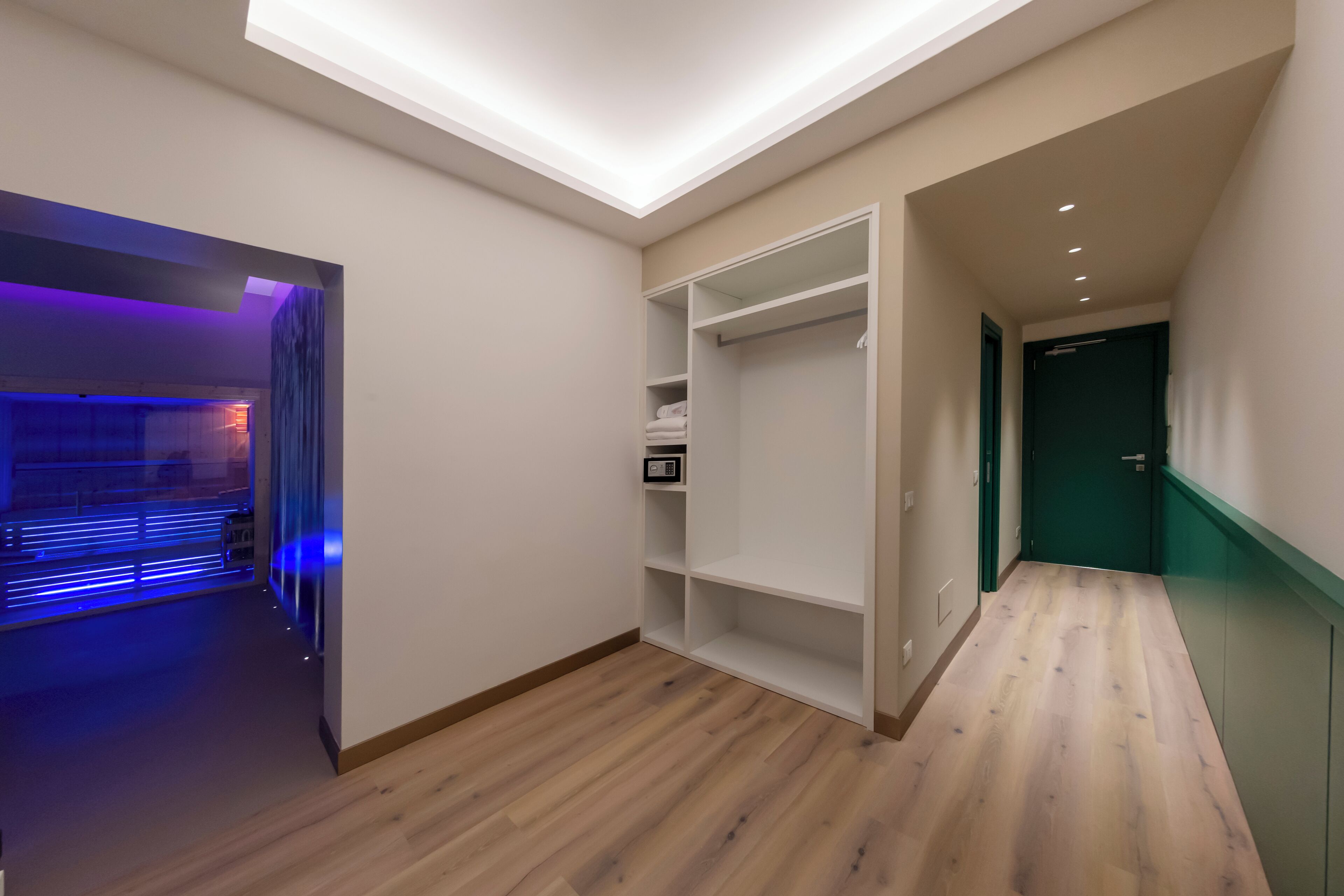 Een moderne hal met houten vloer, een inbouwkast met planken, en een deur naar een andere kamer.