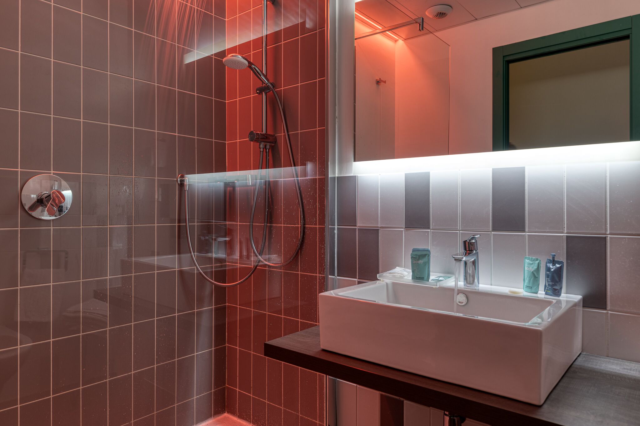 A modern bathroom with a glass-enclosed shower, a white sink with two faucets, and a mirror above the sink.