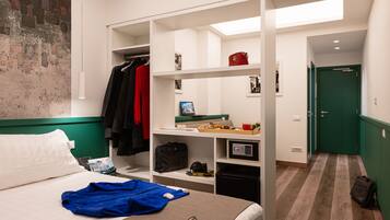 Quarto de hotel com cama, guarda-roupa, escrivaninha com computador e uma porta verde ao fundo.
