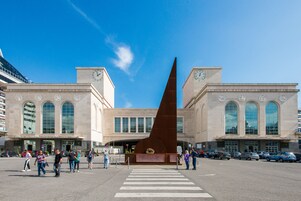 Una stazione ferroviaria con un'alta torre dell'orologio e un monumento imponente al centro.