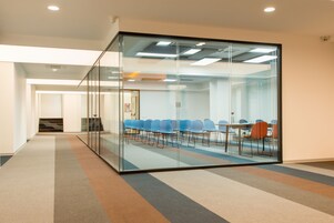 Una sala conferenze con pareti in vetro, pavimento rivestito a moquette e disposizione dei posti a sedere.
