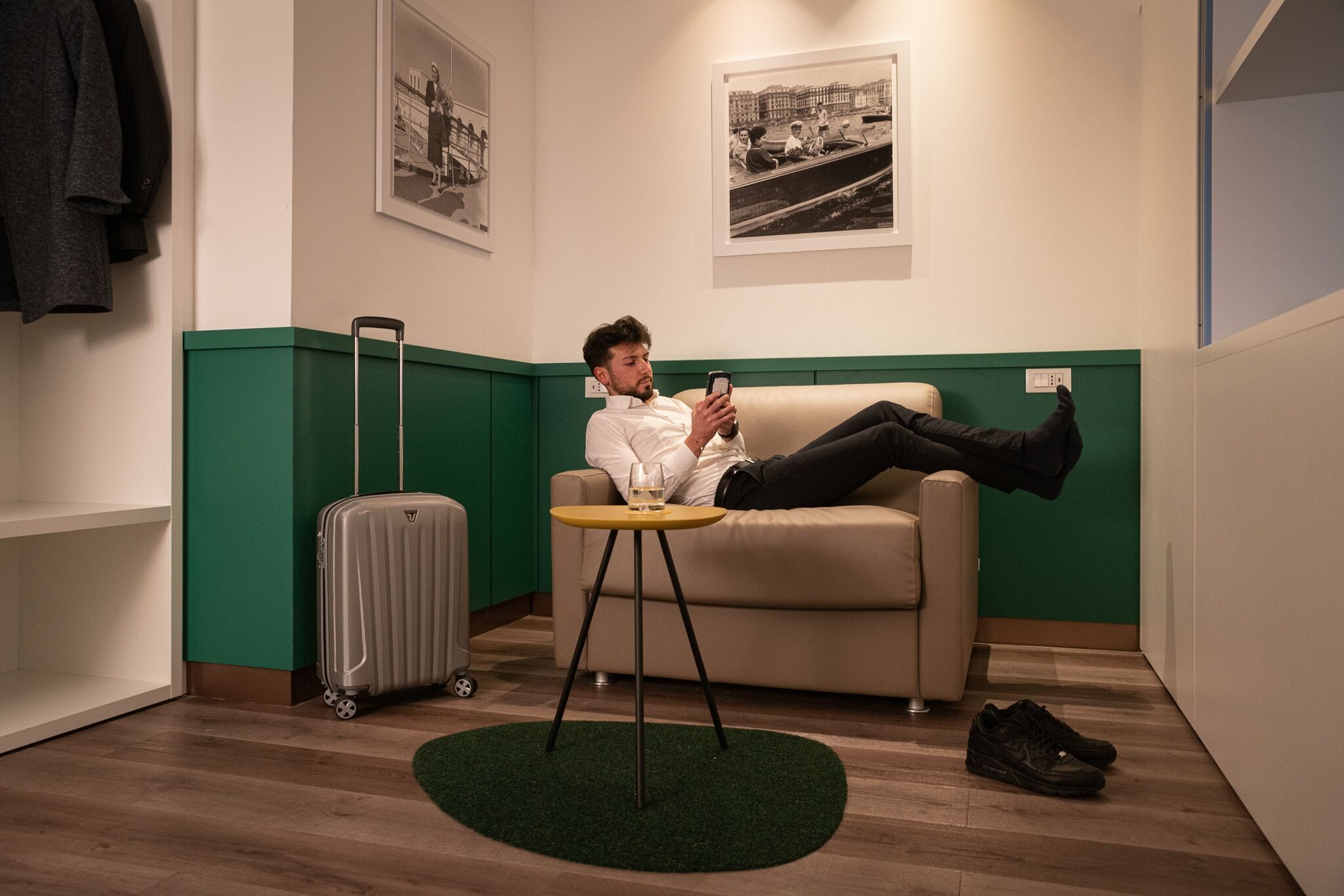 A person lying on a sofa in a room with a suitcase and a pair of shoes on the floor.