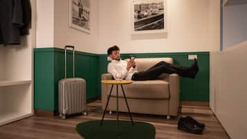 A person lying on a sofa in a room with a suitcase and a pair of shoes on the floor.