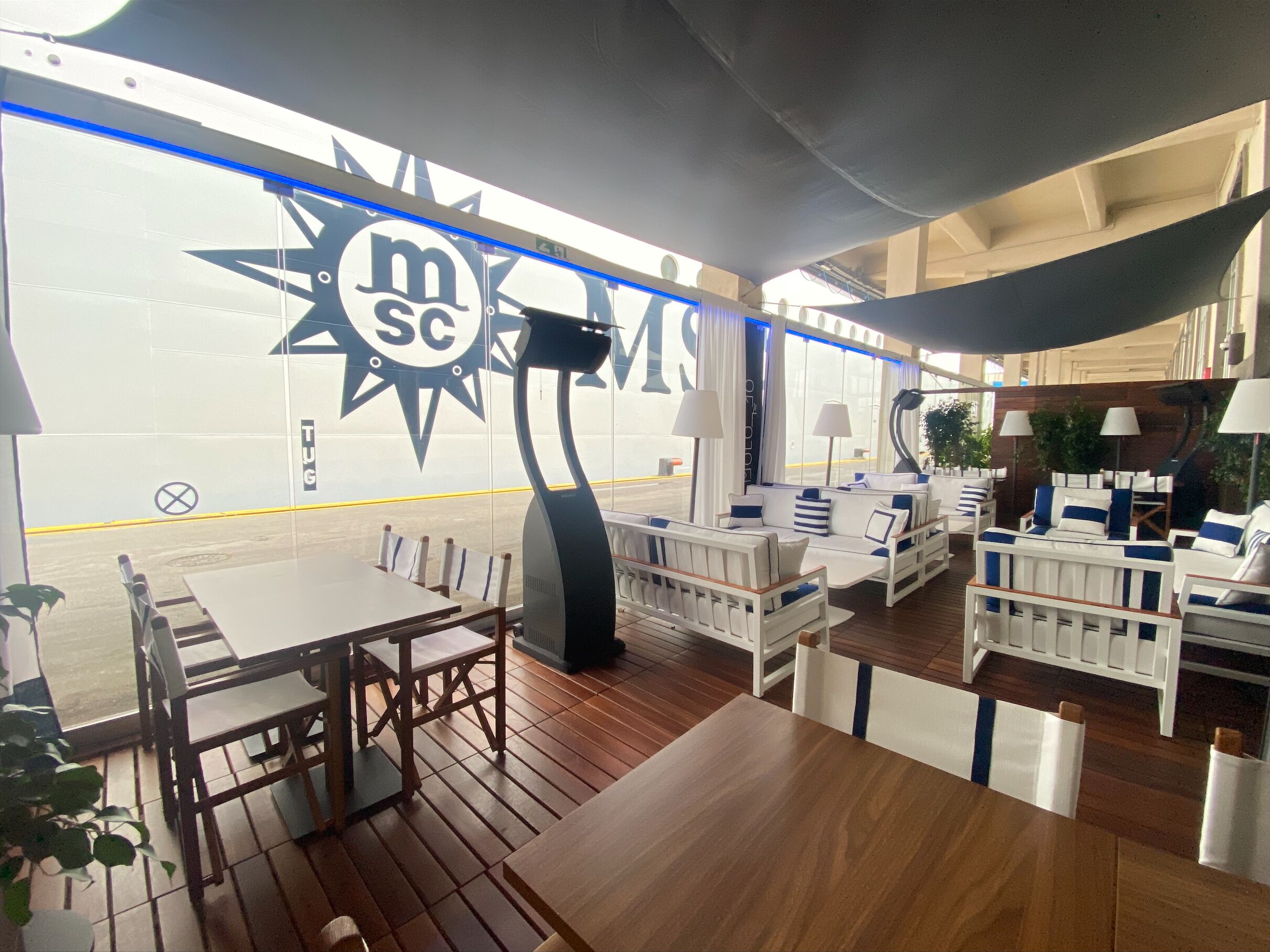 Un restaurante con mesas de madera y asientos acolchados blancos. Se ve un letrero grande con la inscripción 'MSC'.