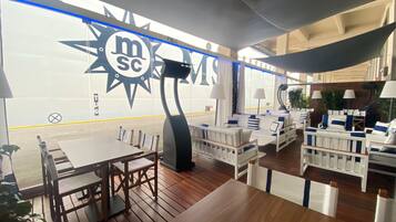 Un ristorante con tavoli in legno e sedute imbottite bianche. Si nota un cartello con la scritta 'MSC'.