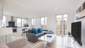 A modern living room with a grey sofa, a white coffee table, and a flat-screen TV. - Spacious 2-Bed · Balcony · St Pancras · Sleeps 6 (London)
