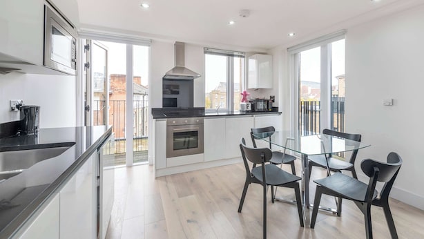 A modern kitchen with a glass dining table and chairs, a built-in oven, and a stainless steel range hood. - Spacious 2-Bed · Balcony · St Pancras · Sleeps 6 (London)