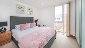 A bedroom with a large bed, a nightstand, a window with curtains, and artwork on the wall. - Spacious 2-Bed · Balcony · St Pancras · Sleeps 6 (London)