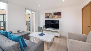 A modern living room with a sofa, a coffee table, a TV, and a sliding glass door leading to a balcony. - Spacious 2-Bed · Balcony · St Pancras · Sleeps 6 (London)