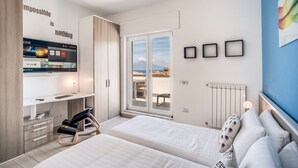 A modern bedroom with two beds, a desk, a TV, and a view of the city. - SeaView Apartment Sorrento center! (Sorrento)