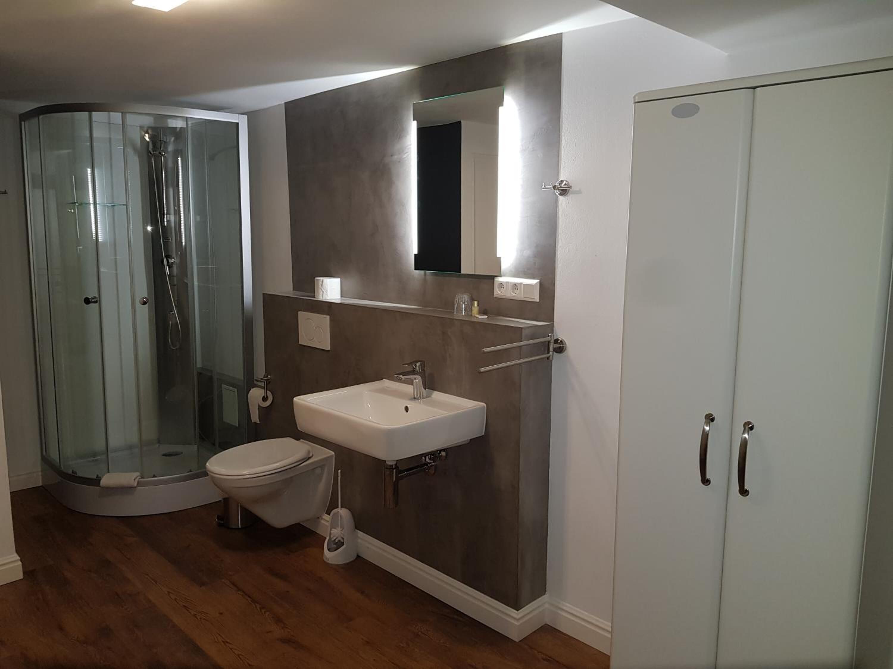 Un bagno moderno con box doccia in vetro, un water, un lavabo e un armadietto.