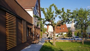 A courtyard with a paved walkway, a tree, and outdoor furniture.