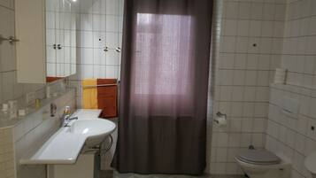 Een badkamer met een witte wastafel, spiegel en toilet. Er is een douchegordijn en een handdoekrek met handdoeken.