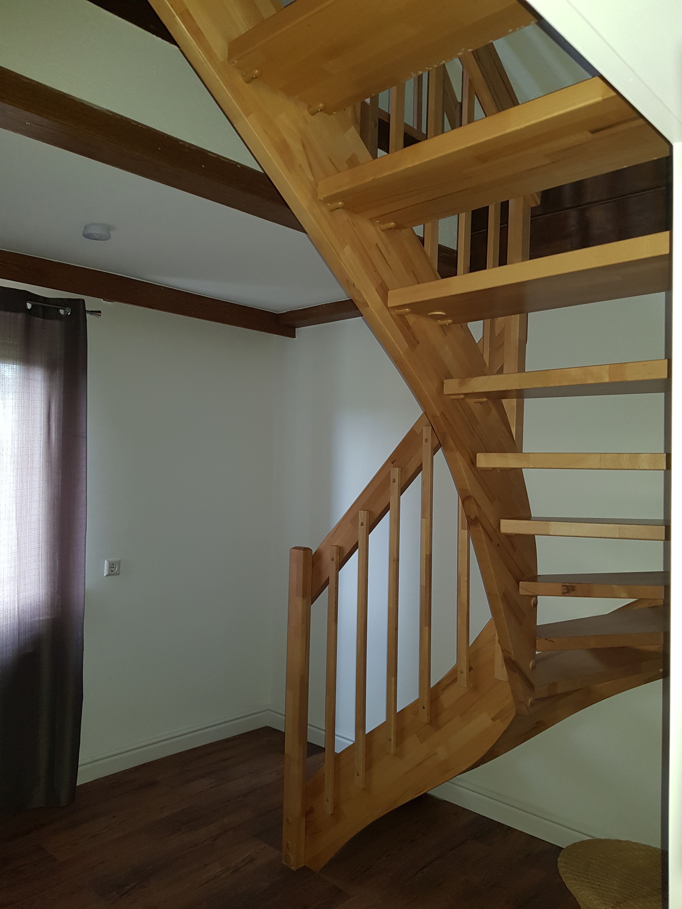 Una escalera de madera con barandilla, una pared blanca lisa y un piso de madera oscura.
