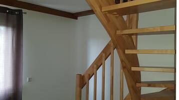 Una escalera de madera con barandilla, una pared blanca lisa y un piso de madera oscura.