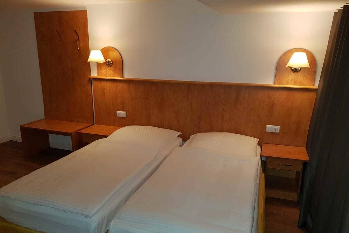 Quarto de hotel com duas camas de solteiro, cabeceiras de madeira, mesas de cabeceira e luminárias fixadas na parede.