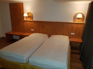 Una habitación de hotel con dos camas individuales, cabeceros de madera, mesitas de noche y lámparas de pared.