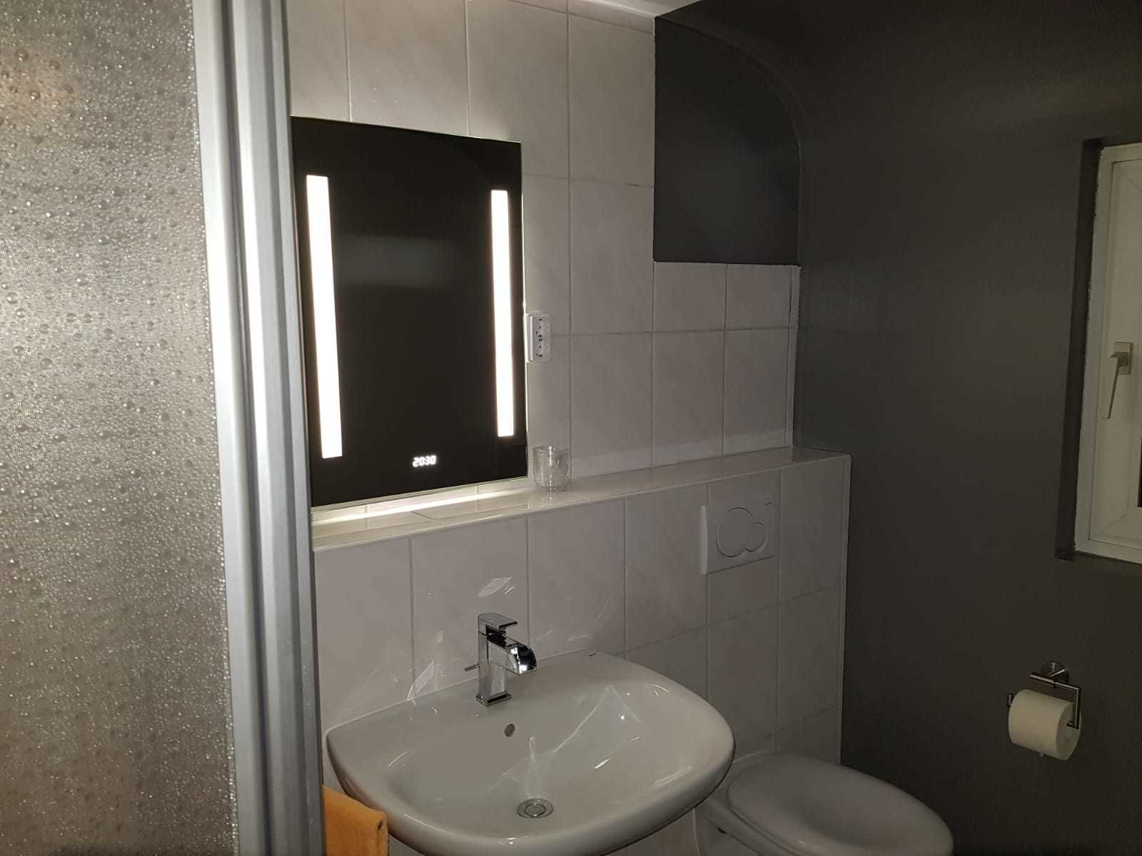 Un baño con lavamanos blanco, espejo y retrete.