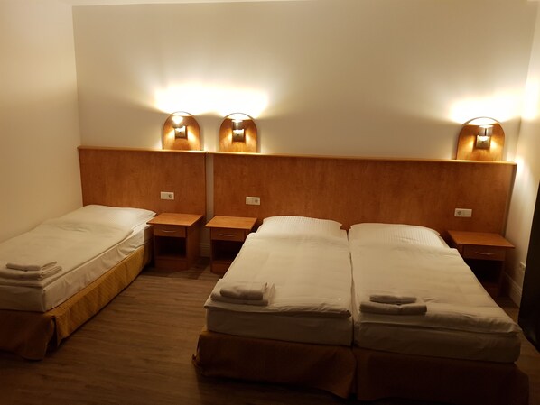 Habitación de hotel con dos camas individuales y dos camas de matrimonio, cada una con cabecero y mesitas de noche de madera.