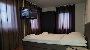 A modern hotel room with a bed, a TV mounted on the wall, and a small table with a remote control.