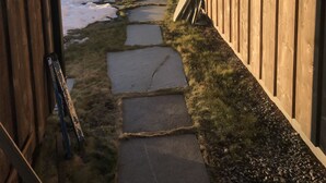 A wooden cabin with a stone pathway leading to a window overlooking a lake and mountains.