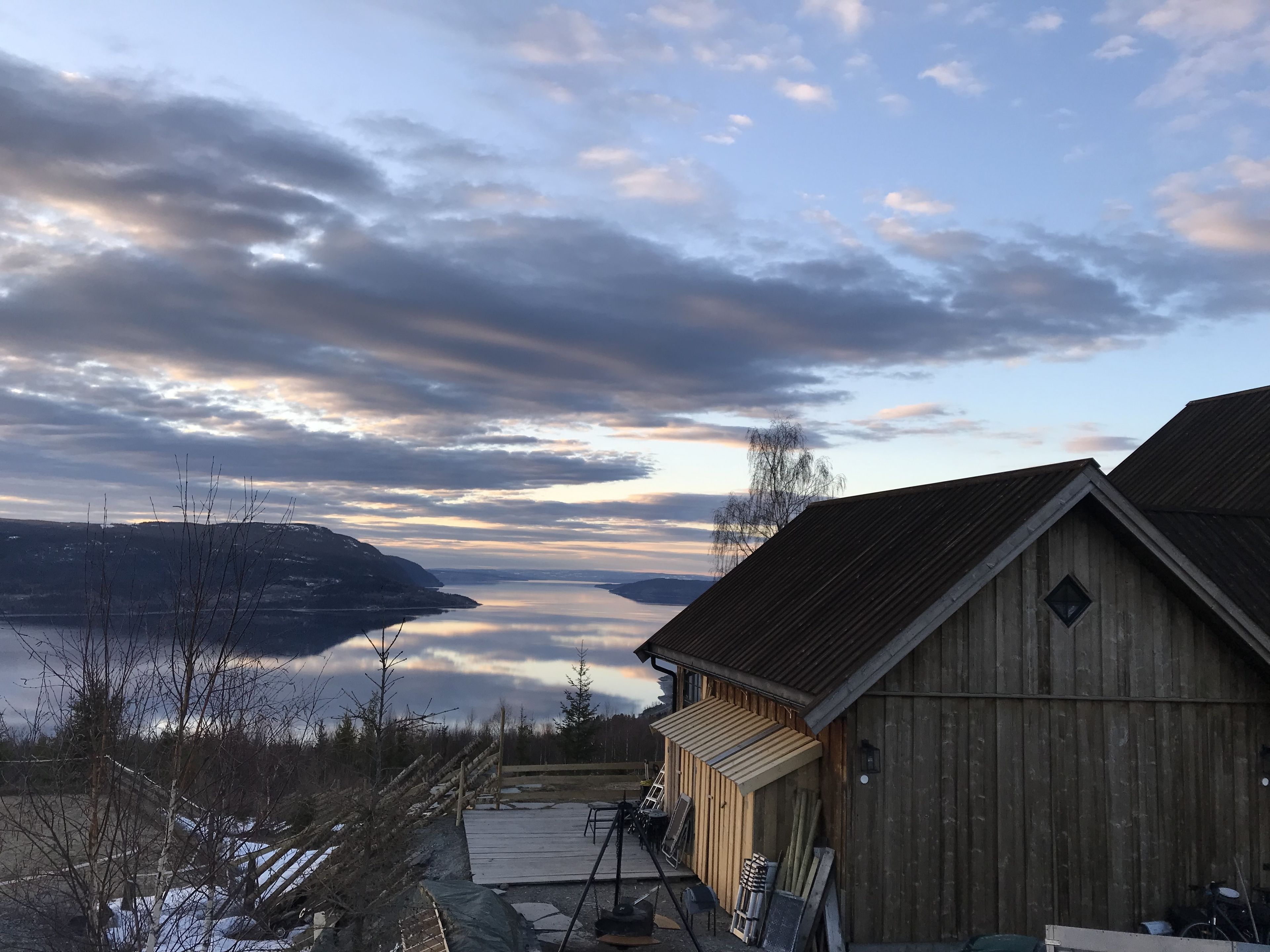 A wooden building with a sloped roof, a dock extending into a body of water, and a mountainous landscape in the background.