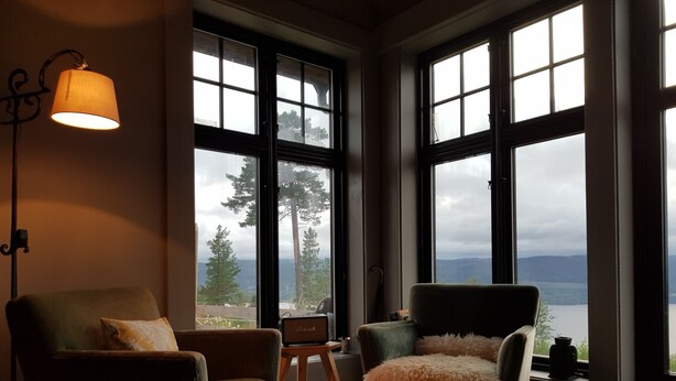 A room with two armchairs, a floor lamp, and large windows offering a view of trees and mountains.