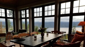 A dining area with a table, chairs, and a view of a lake through large windows.