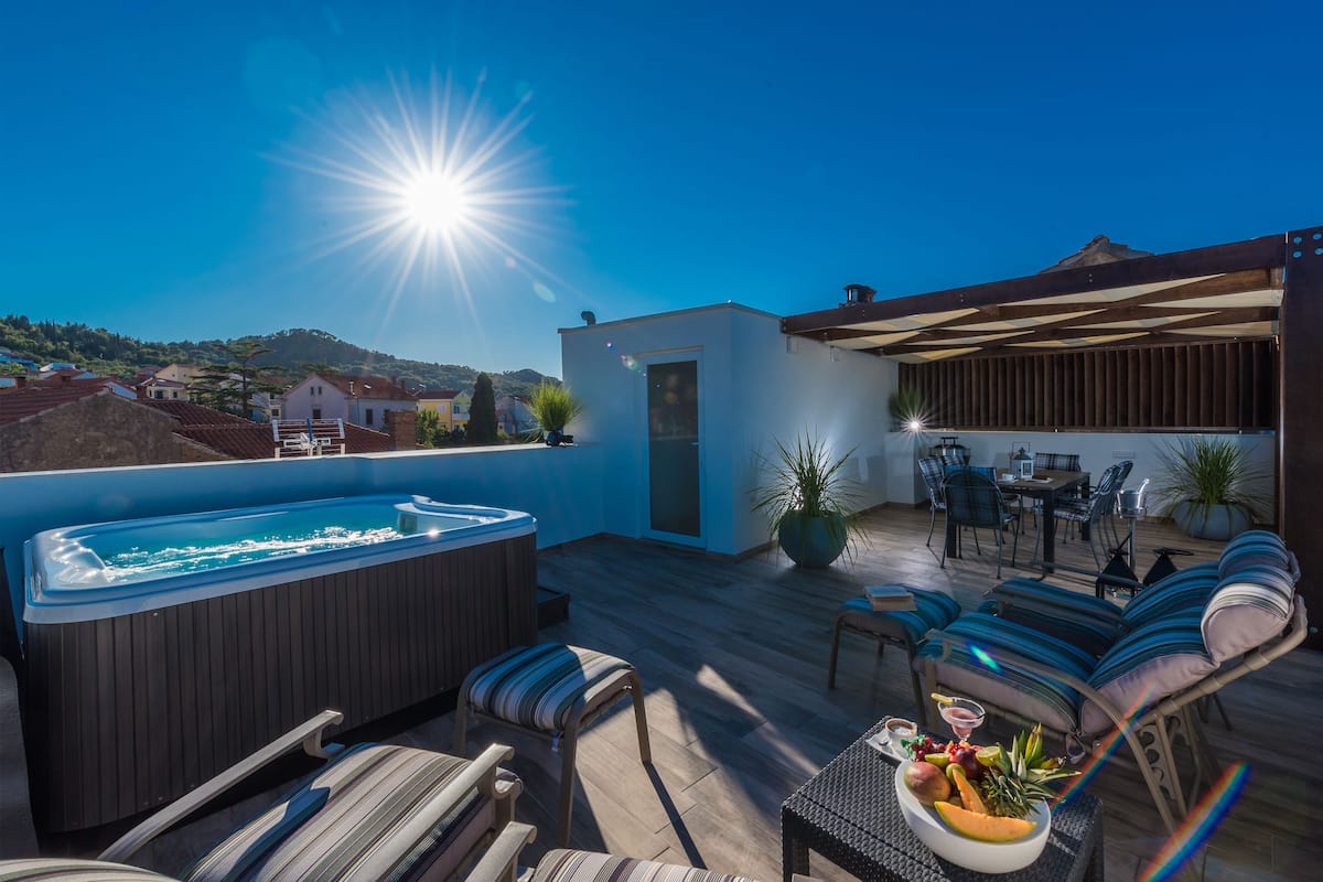 A rooftop terrace with a hot tub, outdoor seating, and a view of the surrounding landscape.
